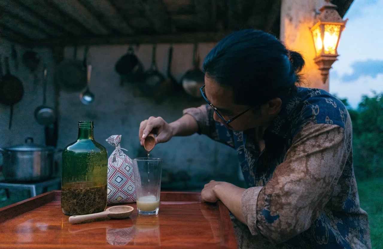 An amber bottle of a herbal blend and a small pouch of sachets resting on a linen cloth by a dusk window ledge